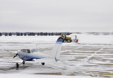 small airplane on runway in winter with snowplow in background