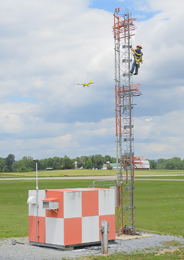 A repair person on the ladder of an airport automated weather observing system